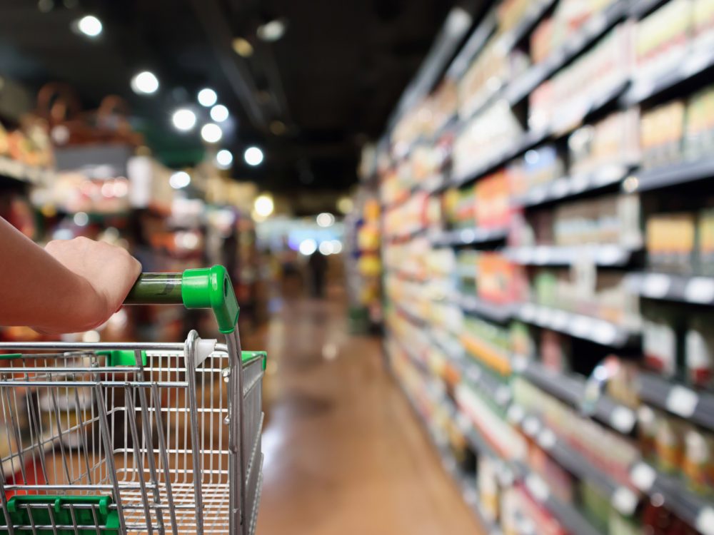 woman hand hold shopping cart with Abstract blur supermarket aisle background